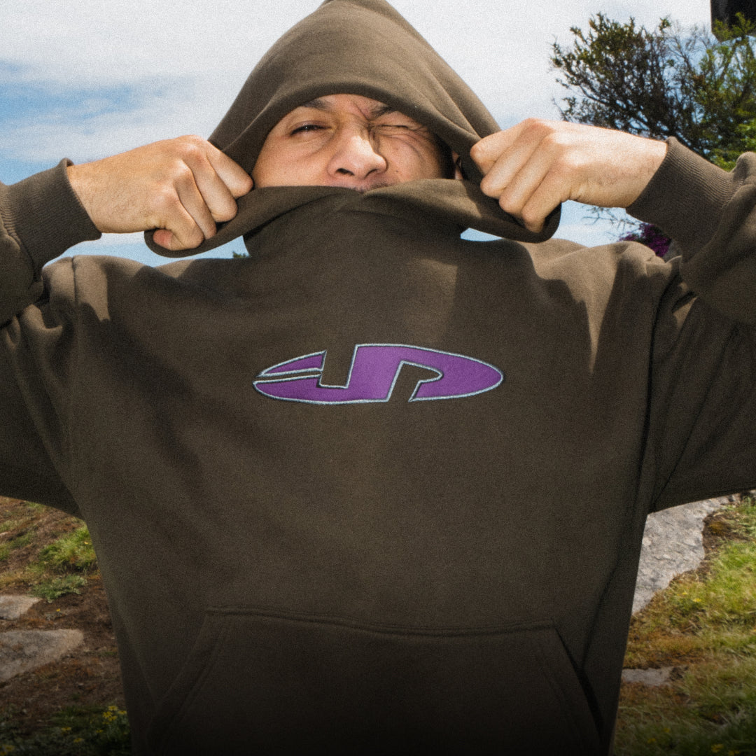 Person wearing a brown hoodie with a purple logo outdoors